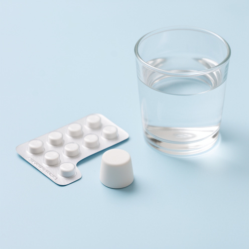 Suppositoire médical blanc présenté avec une plaquette neutre et un verre d’eau sur une surface médicale propre.
